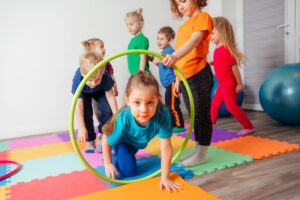 Active kid crawling on colorful mats through hula hoops held by other children.